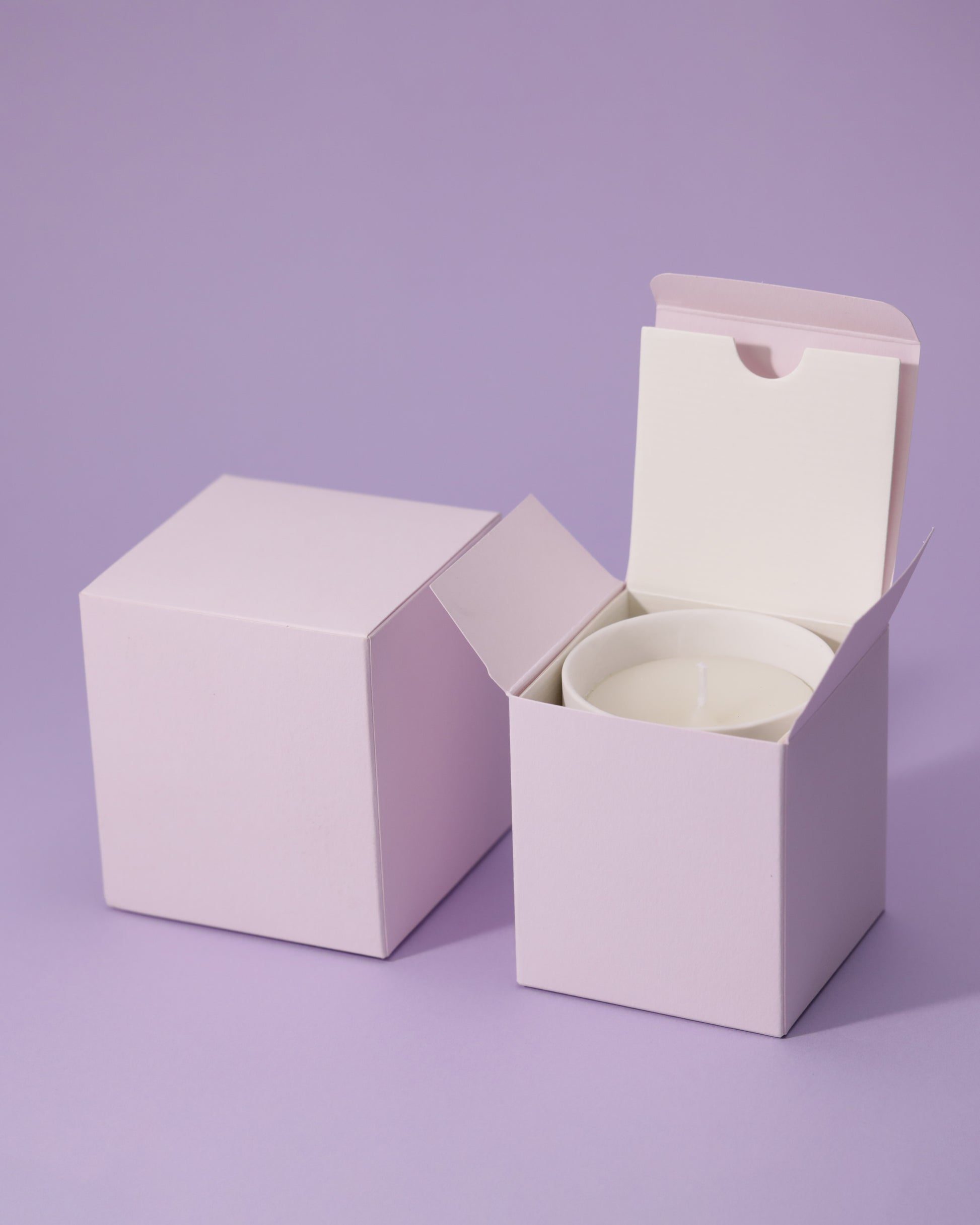Soft lavender square boxes, one open revealing a white candle.