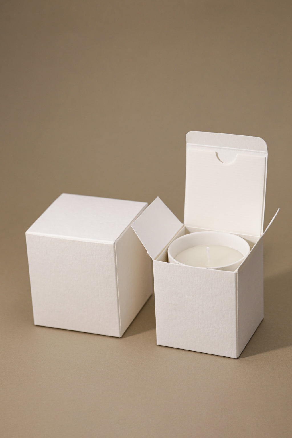 Two white textured candle boxes, one open with a candle inside.