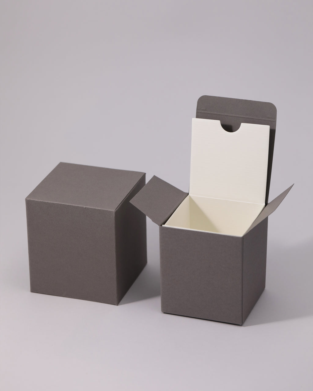 Two dark gray cube boxes, one closed and one open with a cream interior.