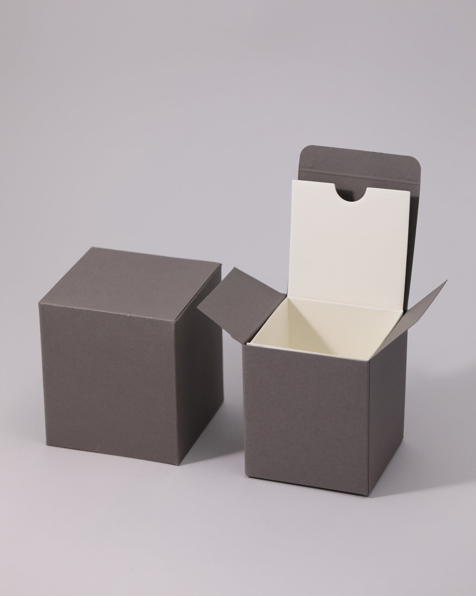 Two dark gray cube boxes, one closed and one open with a cream interior.
