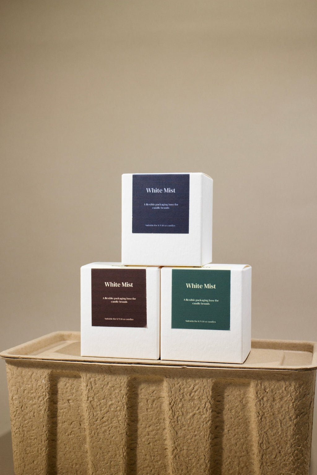 Three white "White Mist" candle boxes with blue, brown, and green labels on a textured tray.